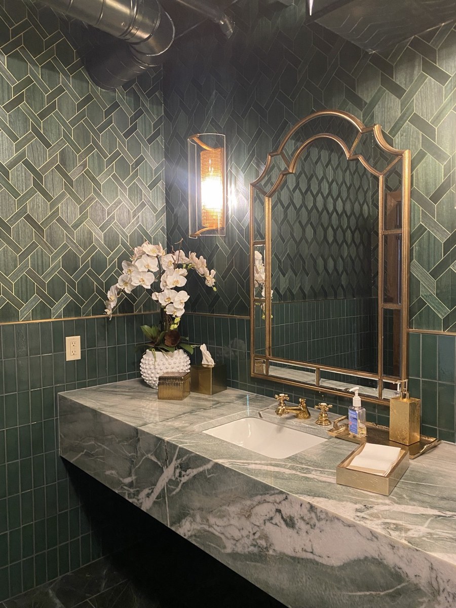 Powder room with emerald green tile, a brass-framed mirror, and a marble vanity